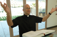 Nicholas Collura reads from a lectionary, dressed for ministry in a Roman collar.