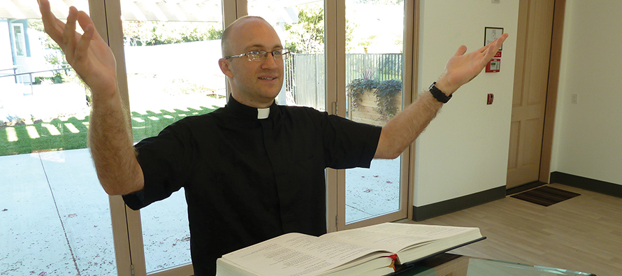 Nicholas Collura reads from a lectionary, dressed for ministry in a Roman collar.