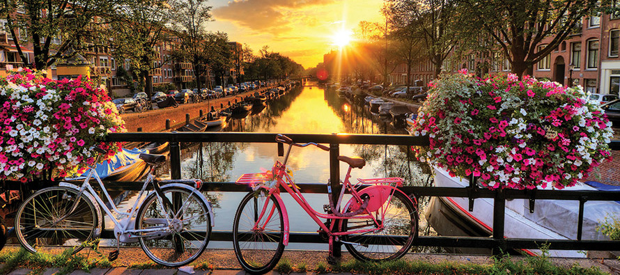 Bicycles parked in front of a canal with the sunset in the background