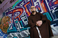 Father M.J. Groark, O.F.M.Cap. sits in front of a wall of graffiti